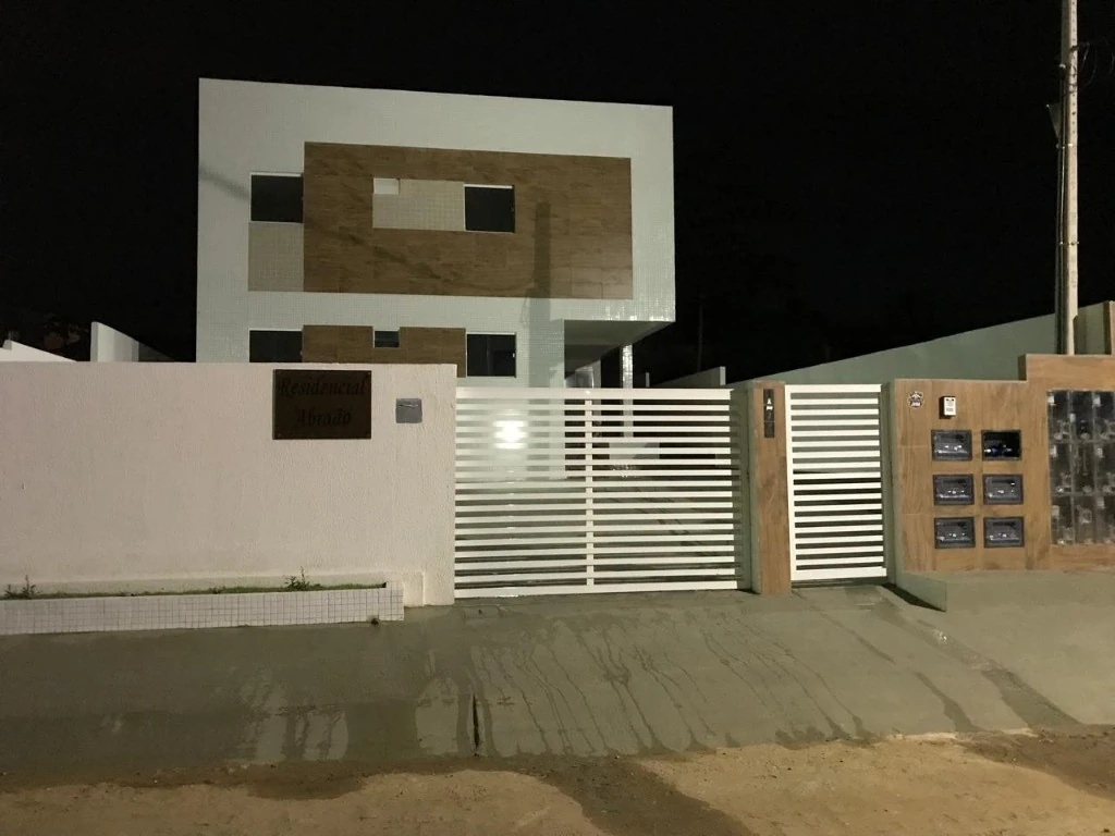 Fachada noturna do Residencial Abraão, edifício residencial de dois pavimentos com revestimento cerâmico e detalhes em madeira